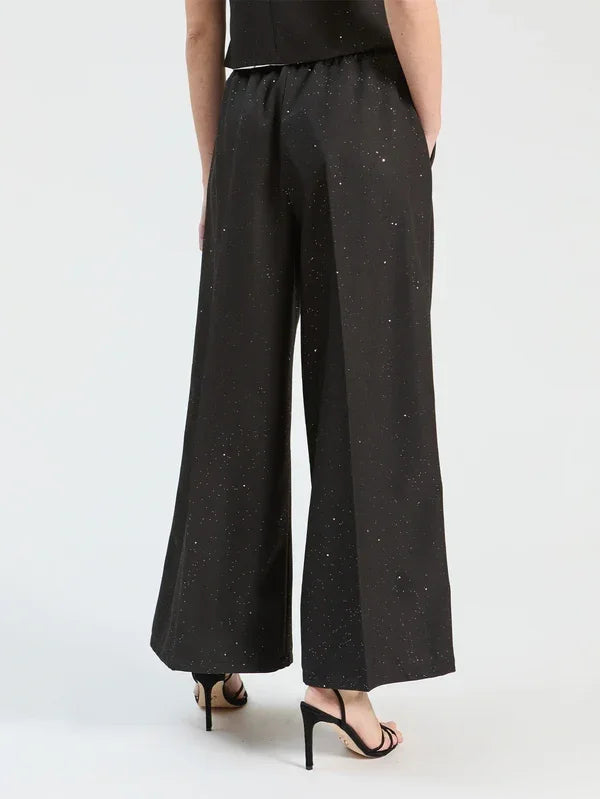 Rear view of a woman wearing black wide-leg trousers with subtle silver shimmer and black heels