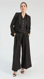 Woman wearing a black three-piece sparkling suit with wide-leg trousers, vest, and blazer.