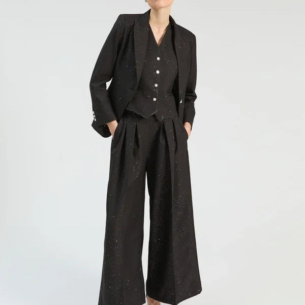 Woman wearing a black three-piece sparkling suit with wide-leg trousers, vest, and blazer.