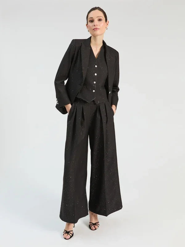 Woman wearing a black three-piece sparkling suit with wide-leg trousers, vest, and blazer.