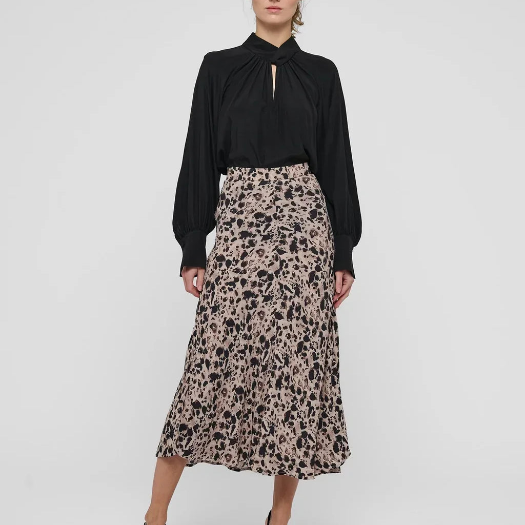 Woman wearing a black long-sleeve blouse and a patterned midi skirt with black pumps.
