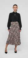 Woman wearing a black long-sleeve blouse and a patterned midi skirt with black pumps.
