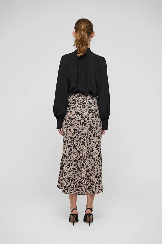 Woman wearing a black long-sleeve blouse and a pink and black animal print midi skirt.