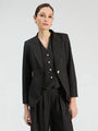 Woman wearing a black three-piece suit with subtle white speckles, including a blazer, vest, and trousers.