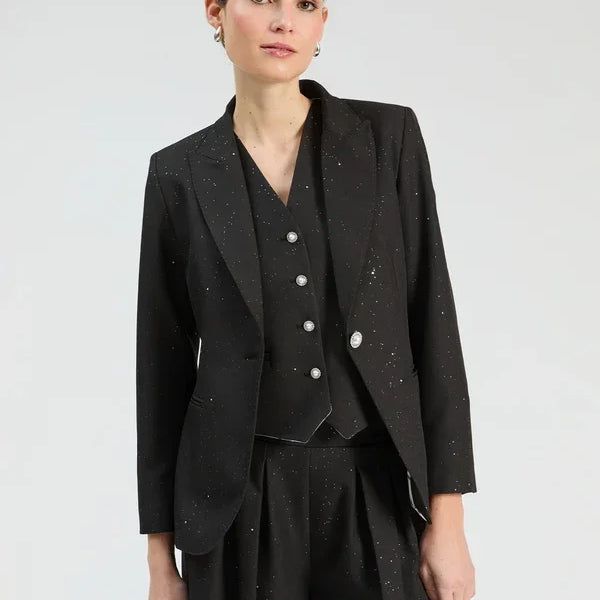 Woman wearing a black three-piece suit with subtle white speckles, including a blazer, vest, and trousers.