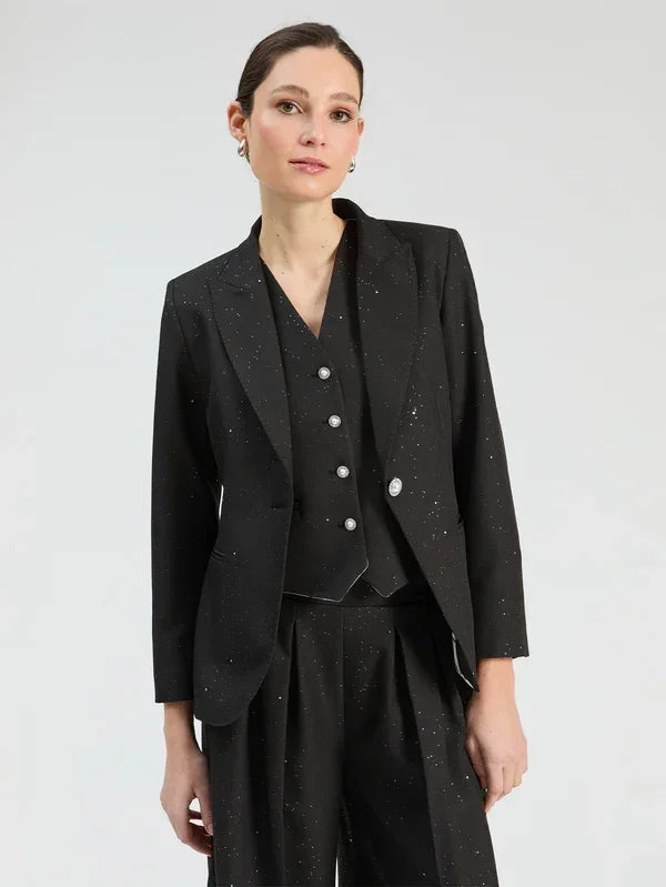 Woman wearing a black three-piece suit with subtle white speckles, including a blazer, vest, and trousers.